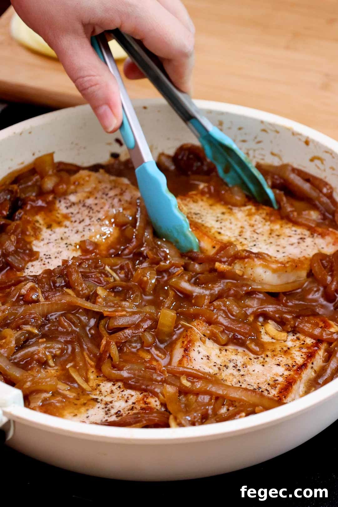 French Onion Pork Chops with Melted Gruyère and Caramelized Onions 10 Tongs placing pork chops into a skillet with caramelized onion sauce.