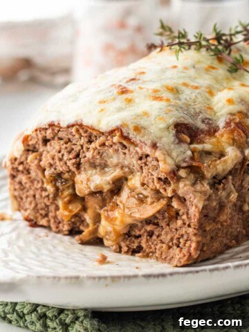 Cooked meatloaf stuffed with mushrooms and cheese on white platter with thyme on top.