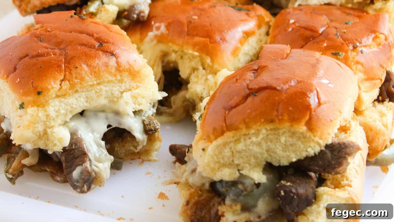 Close-up of beef and cheese sliders with toasted buns on a white surface.