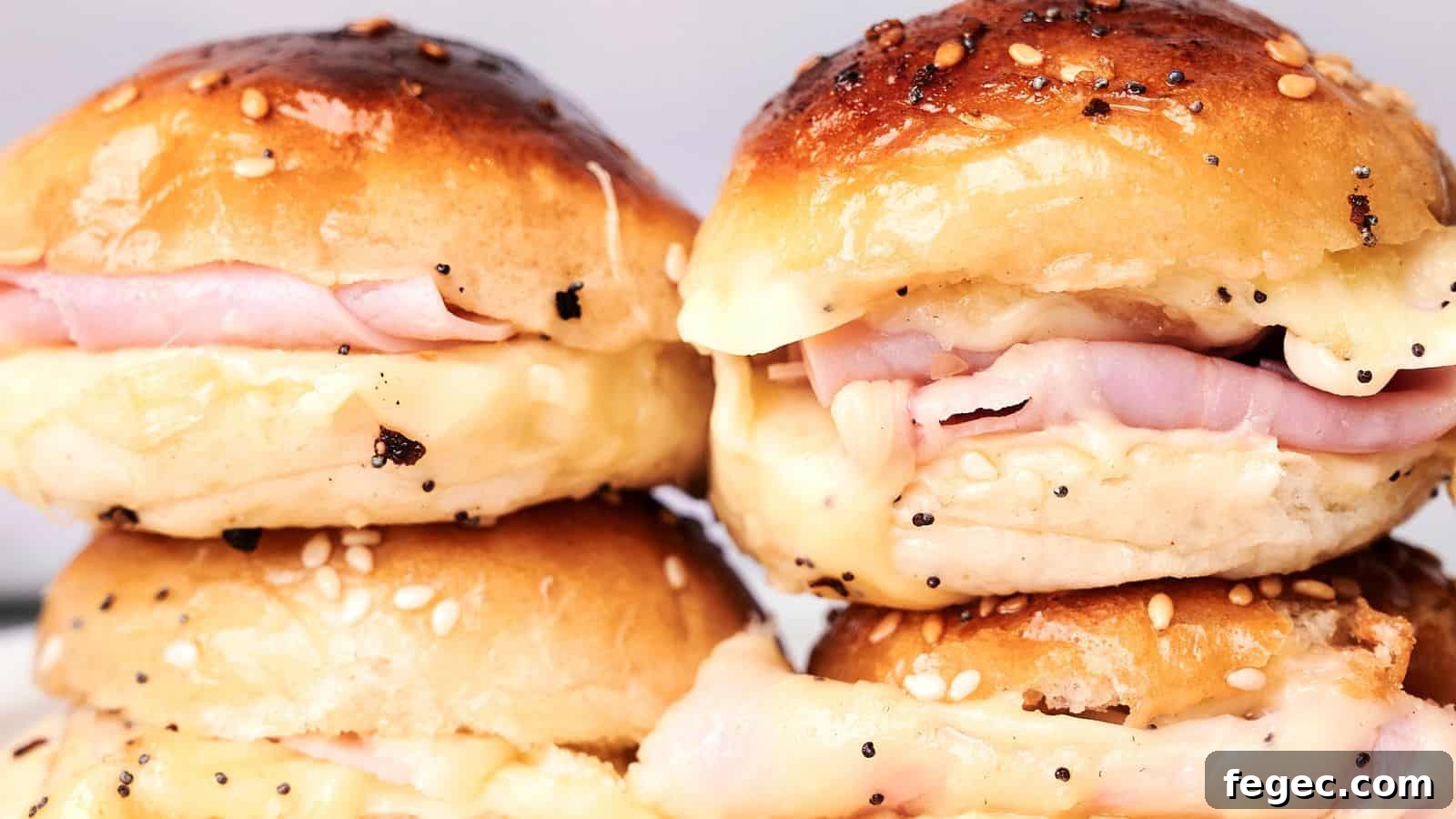 Close-up of four ham and cheese sliders on sesame seed buns, arranged in two stacks. The cheese is melting and oozing out of the sides, making these Ham and Cheese Sliders irresistible.