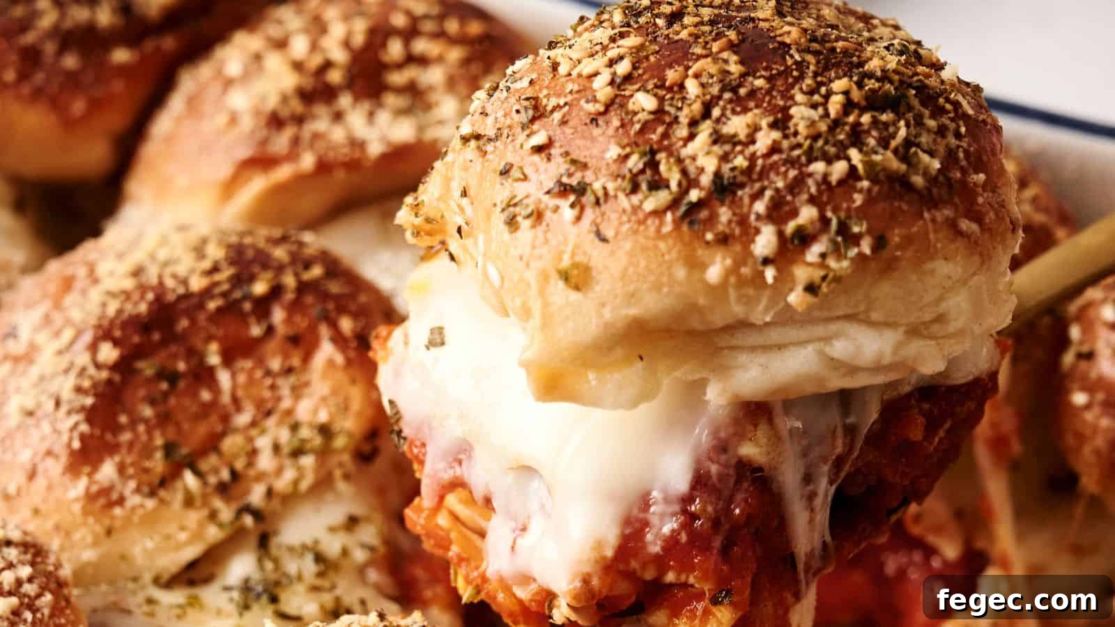 Close-up of a cheesy meatball slider with a seasoned bun, showing melted cheese and tomato sauce. Other sliders are visible in the background.