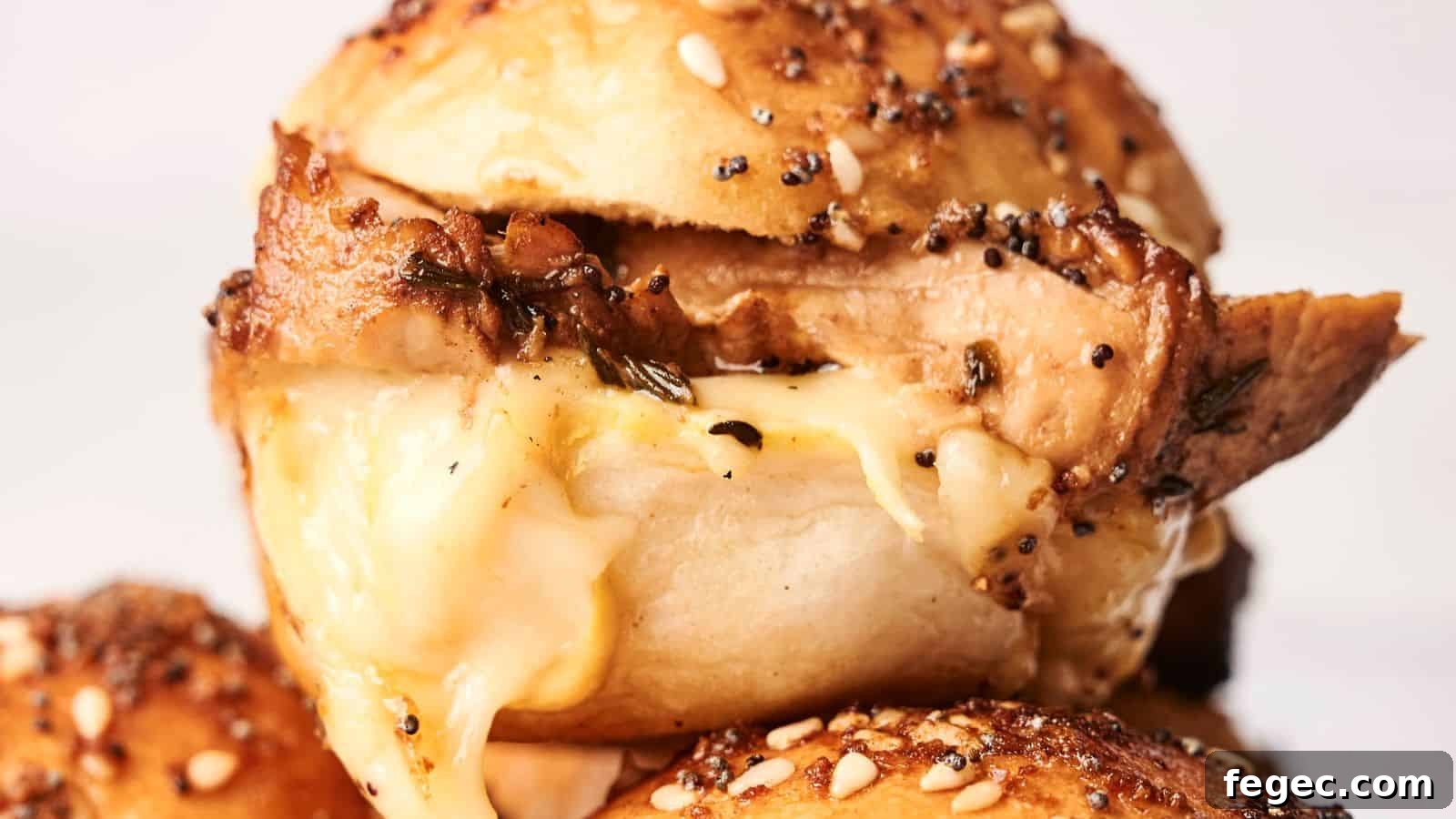 Close-up of a seasoned bagel sandwich with melted cheese and turkey slider filling, topped with seeds.