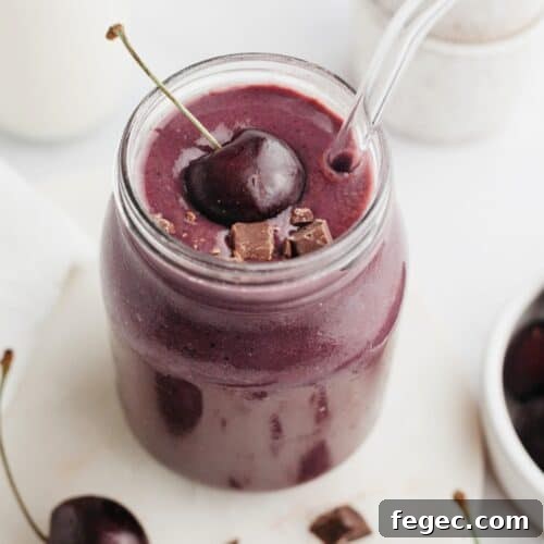 A chocolate cherry smoothie in a glass jar, it is topped with a fresh cherry.