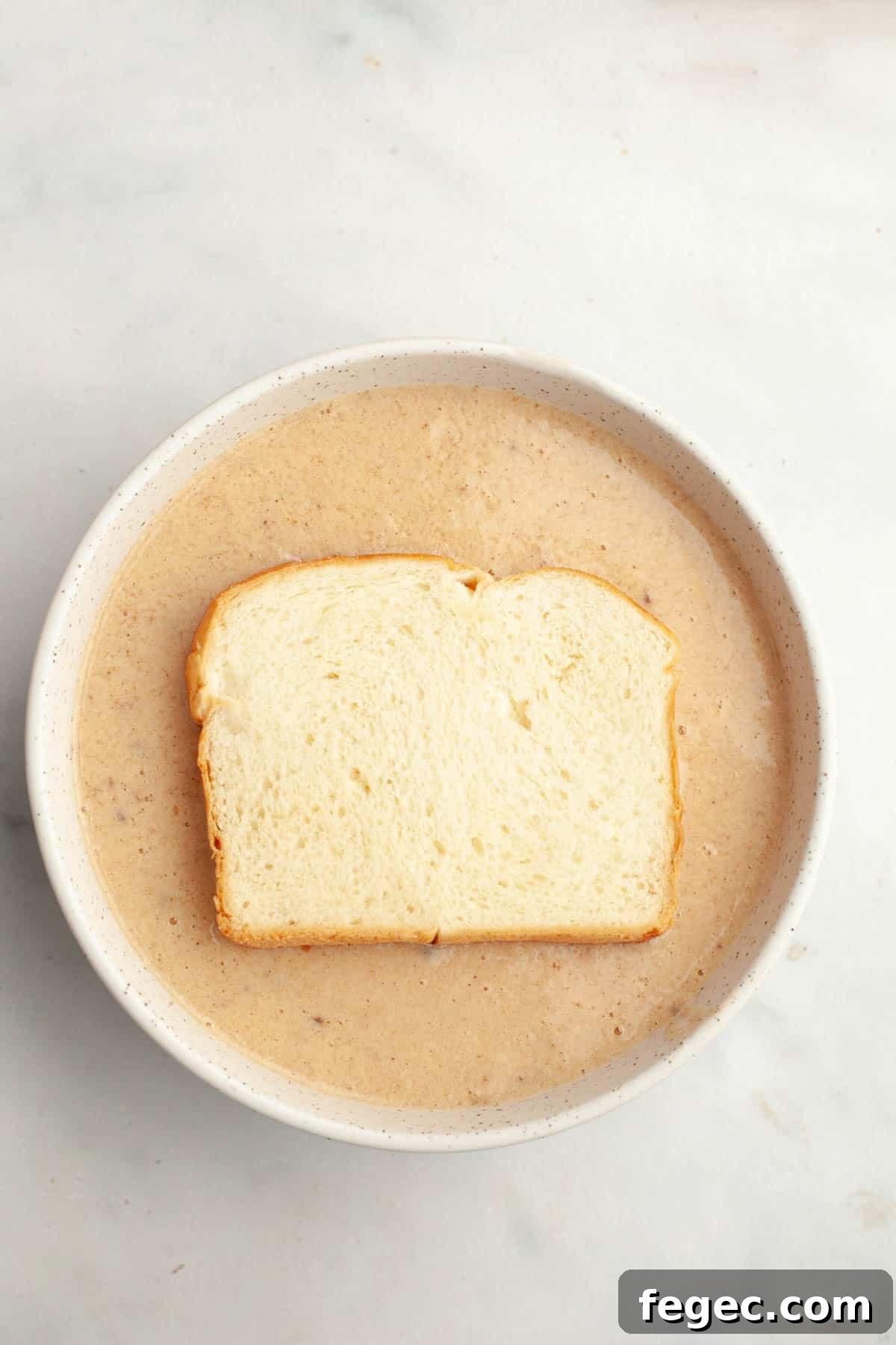 A slice of brioche in a bowl of french toast mixture.