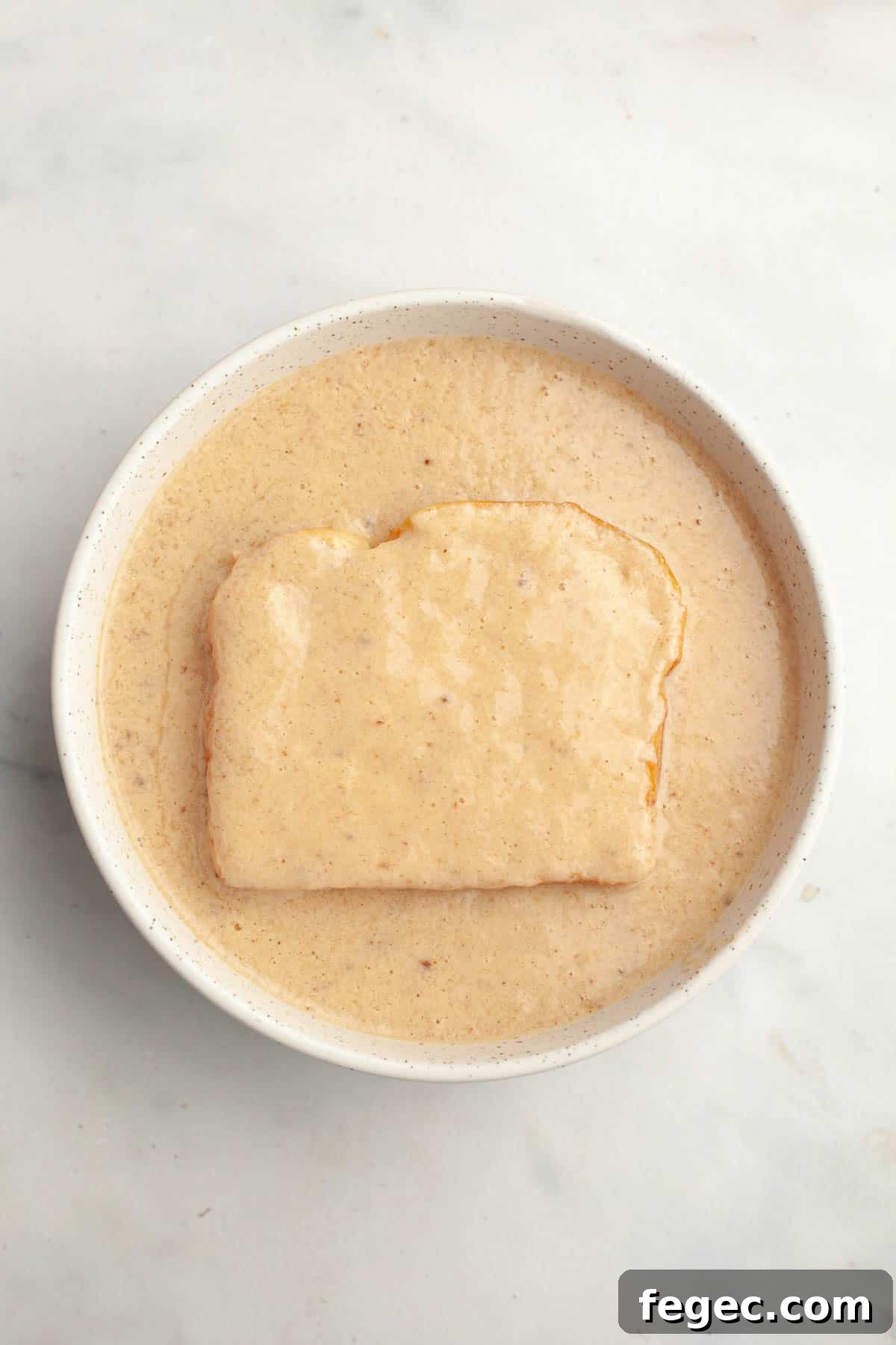 A slice of brioche in a bowl of french toast mixture.