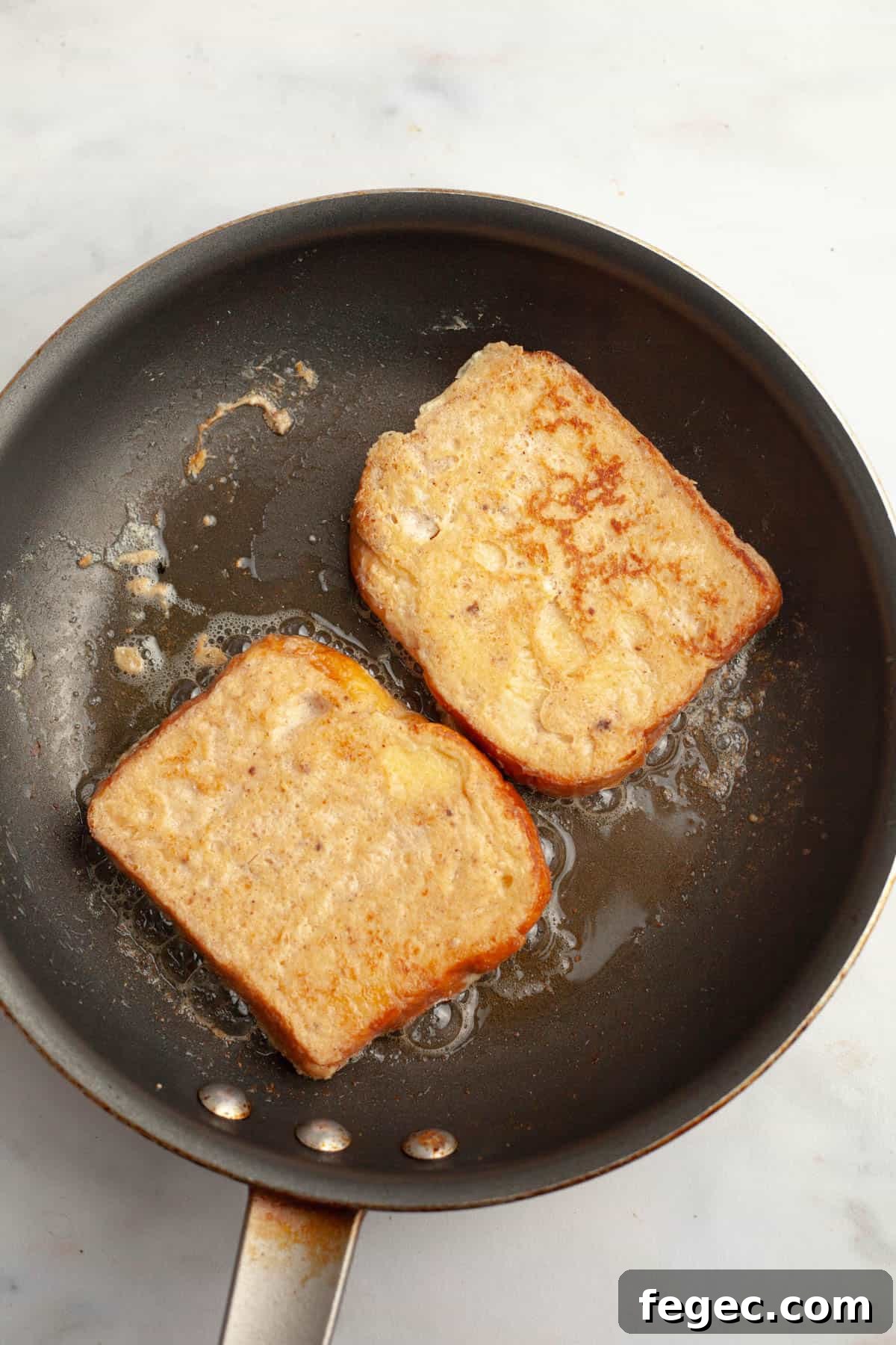 A skillet with two slices of french toast being cooked.