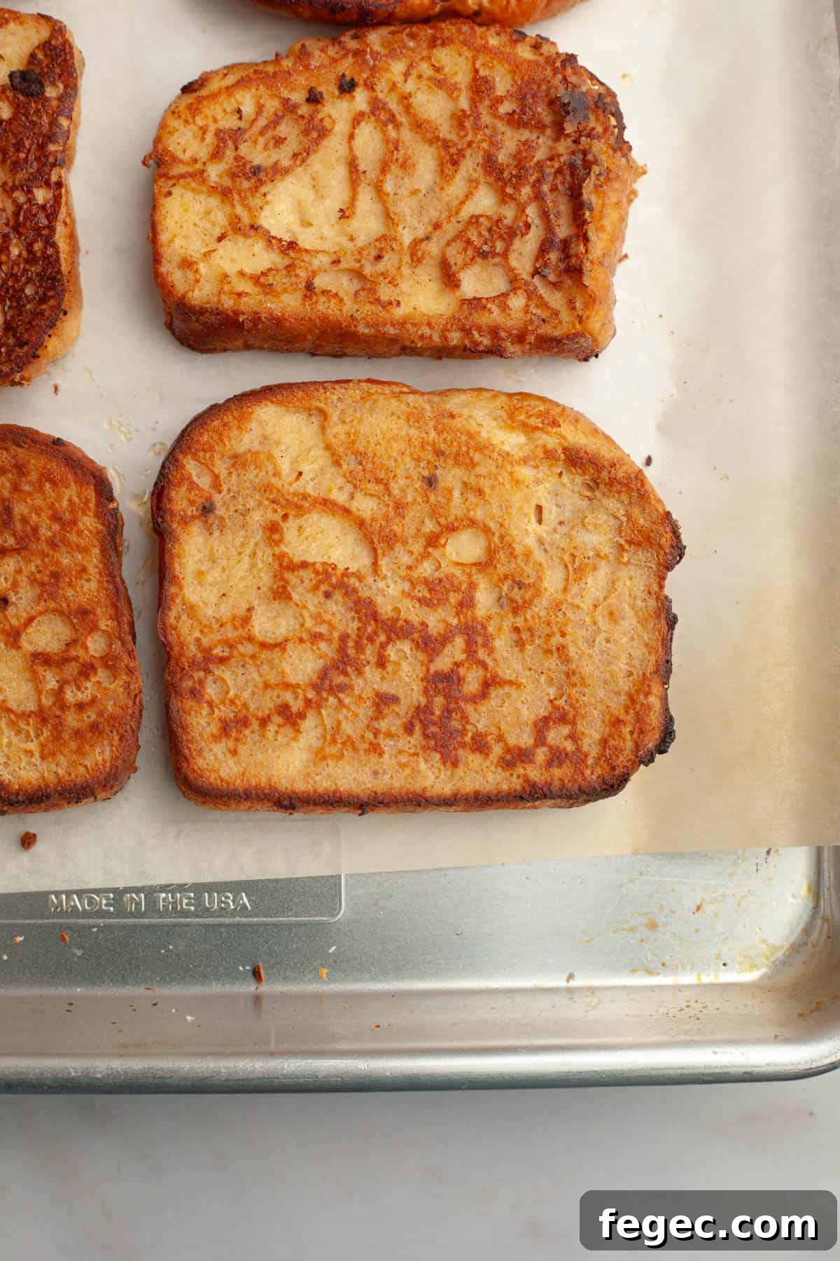 Slices of buttermilk french toasted on a parchment lined baking sheet.