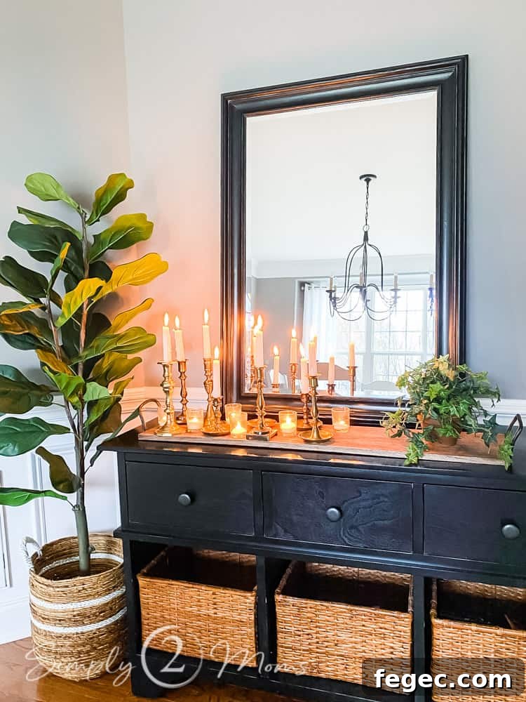 Spring Dining Room Ideas for Greenery Lovers 8 buffet table with mirror above reflecting dining room table and windows. tall faux fiddle leaf plant in basket next to table. candles lit on top of wood tray on table and faux plant next to candle display