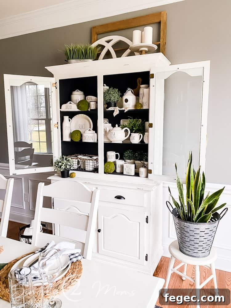 Spring Dining Room Ideas for Greenery Lovers 9 view of china cabinet over corner of dining room table with snake plant in galvanized container on top of wood stool next to china cabinet