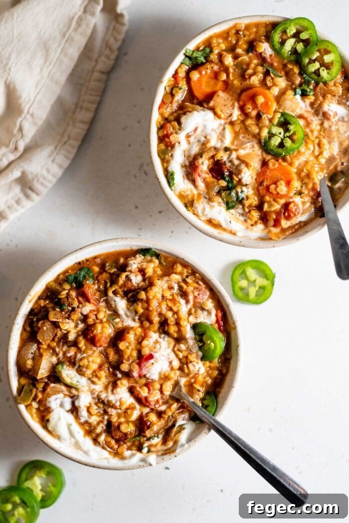 Two bowls of red lentil chili topped with sour cream and sliced jalapeños.