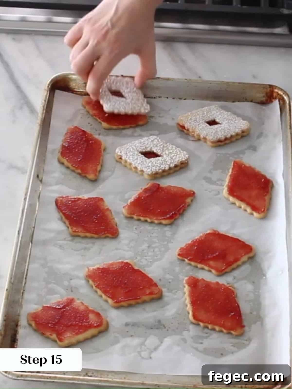Assembled Linzer cookies being finished with top halves showing jam through the center cutouts.