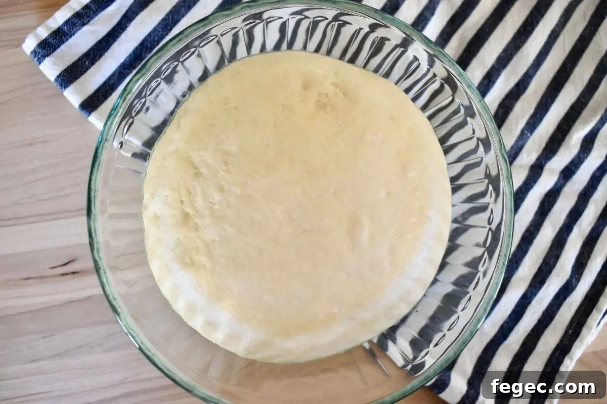Small batch pizza dough in a glass mixing bowl on top of a striped napkin.
