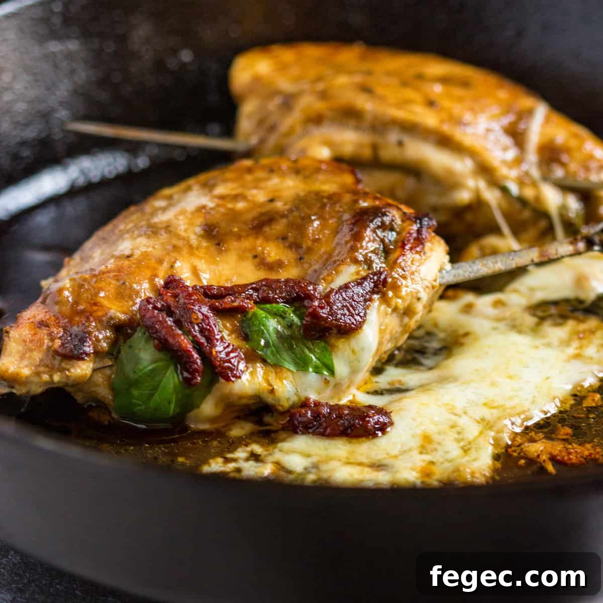 stuffed chicken caprese cooking in a skillet with melted mozzarella and sun-dried tomatoes