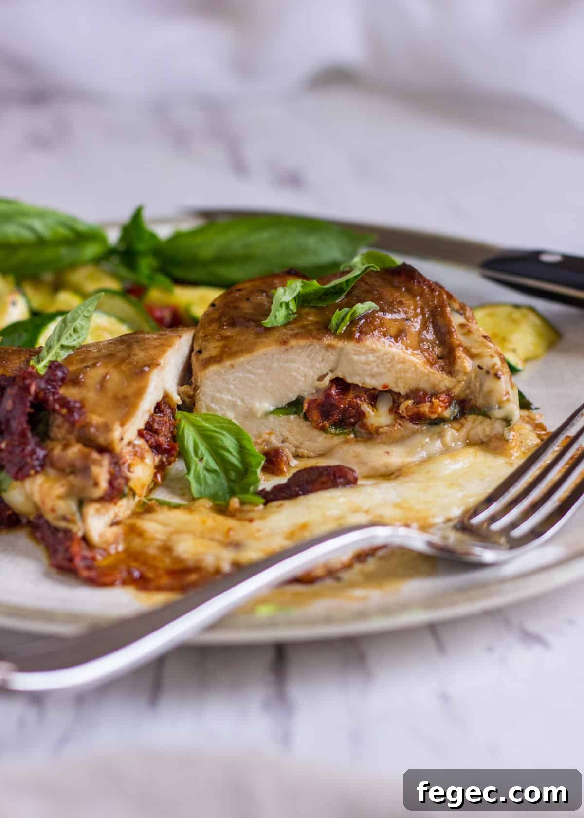 closeup: stuffed chicken caprese cut in half with the fillings showing on a white plate with a fork