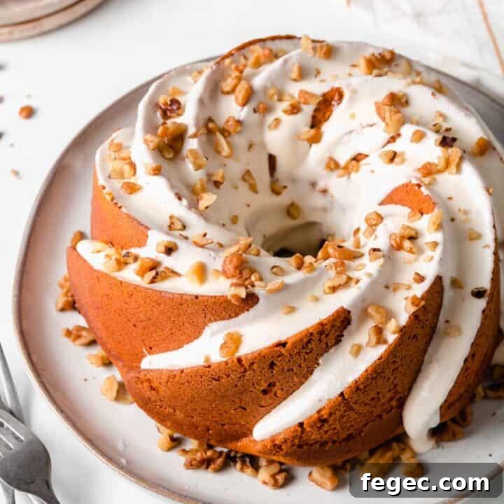 Gluten-free pumpkin bundt cake with frosting dripping down the sides, sprinkled with chopped walnuts.