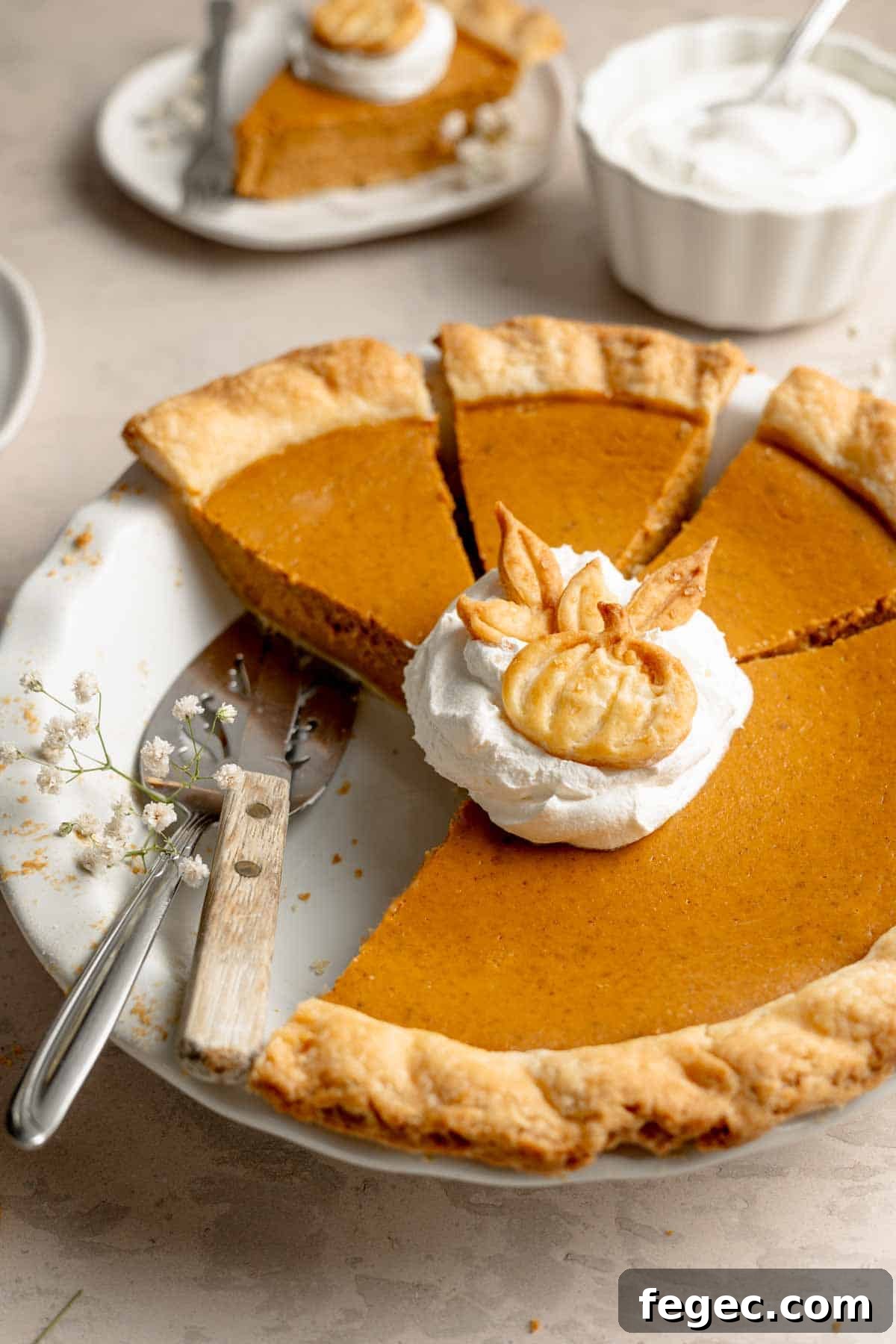 A sliced gluten free pumpkin pie with a dollop of cool whip and pumpkin shaped pie crust cutout.