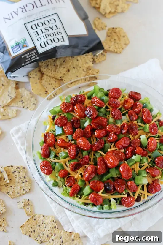 A lighter yet jam-packed with flavor healthier layered taco dip recipe. Colorful, fresh and a crowd-pleasing favorite! A glass pie dish filled with Healthy Taco Dip with a bag of chips in the background.
