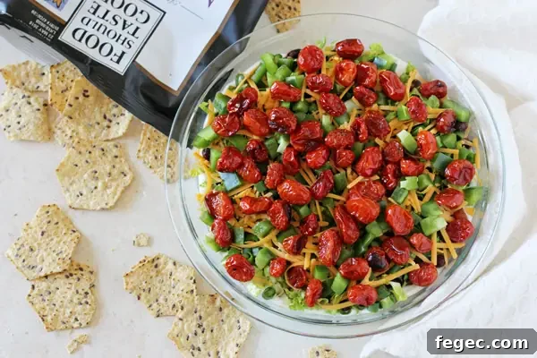 A lighter yet jam-packed with flavor healthier layered taco dip recipe. Colorful, fresh and a crowd-pleasing favorite! A glass pie dish with Healthy Seven Layer Dip with a bag of chips to the side.