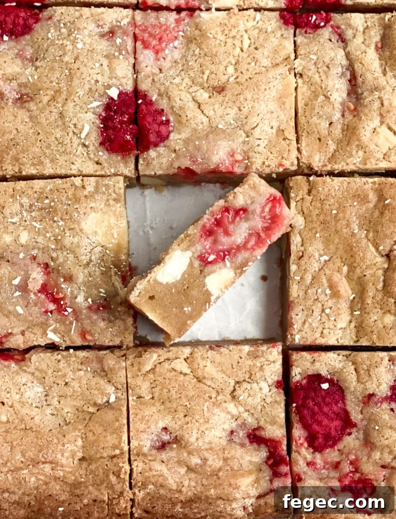 White Chocolate Raspberry Blondies Recipe — Chewy Fruity Bars 16 close up of white chocolate raspberry blondies with one sticking out to see the inside.