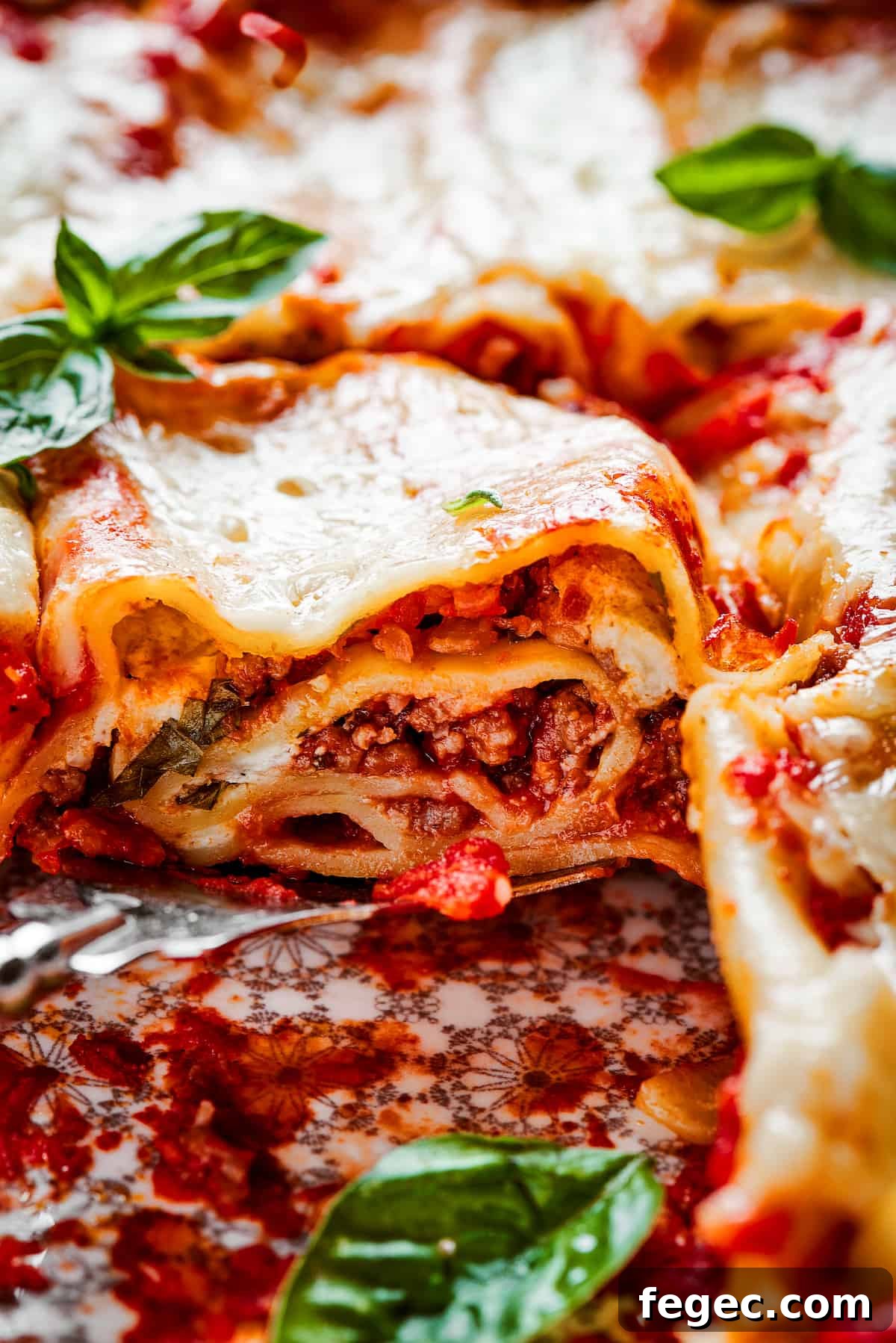 Cheesy Lasagna Roll-Ups Recipe for Family Dinners 4 Close up of a lasagna roll up on a plate topped with basil.