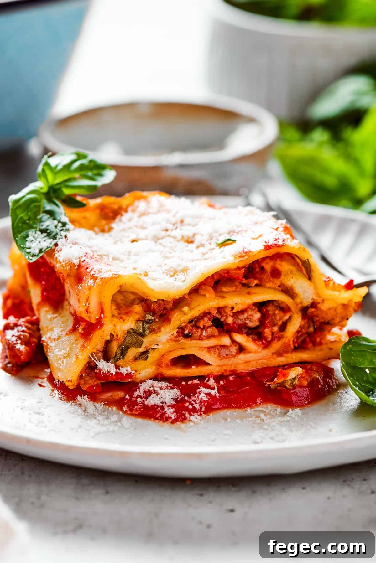 Easy lasagna roll ups have a beefy and herbaceous tomato sauce, a creamy cheese filling, tender pasta, and tons of melted cheese. Lasagna roll up served on a white dinner plate and garnished with fresh basil leaves.
