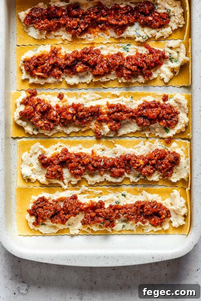 Easy lasagna roll ups have a beefy and herbaceous tomato sauce, a creamy cheese filling, tender pasta, and tons of melted cheese. Overhead view of lasagna noodles covered with a cheese mixture and a ragu.