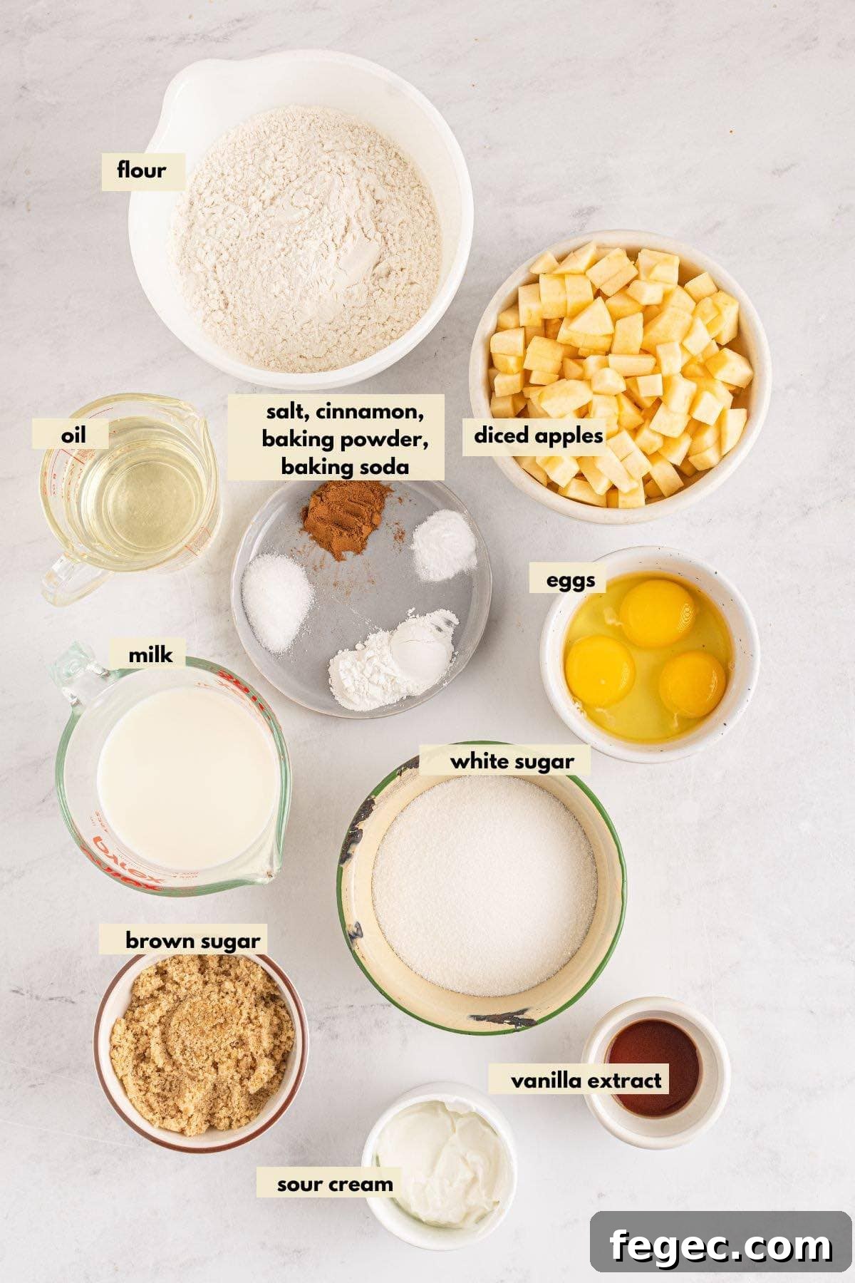 Ingredients to make apple muffins including apples, cinnamon, brown sugar, eggs, flour, oil, sour cream.