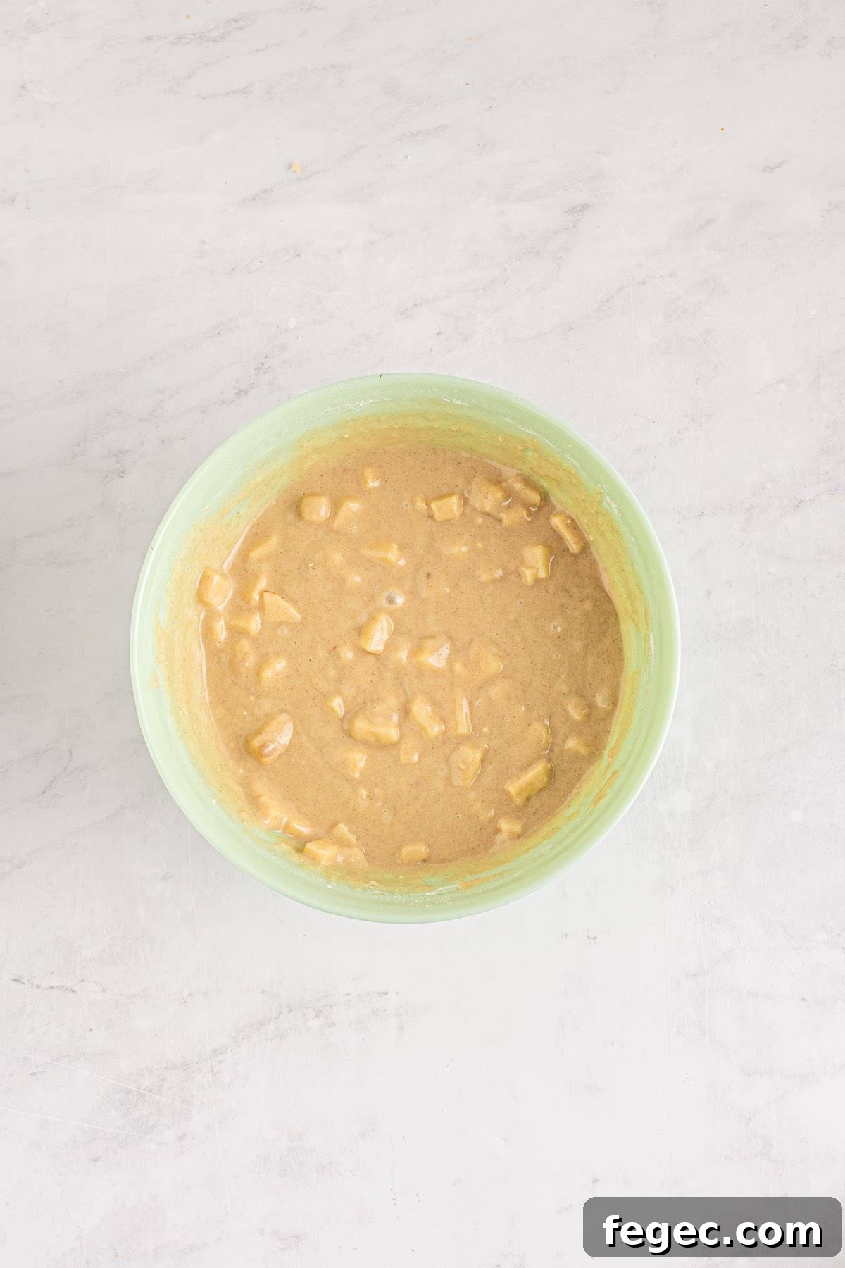 A mixing bowl with muffin batter and apple pieces in it.