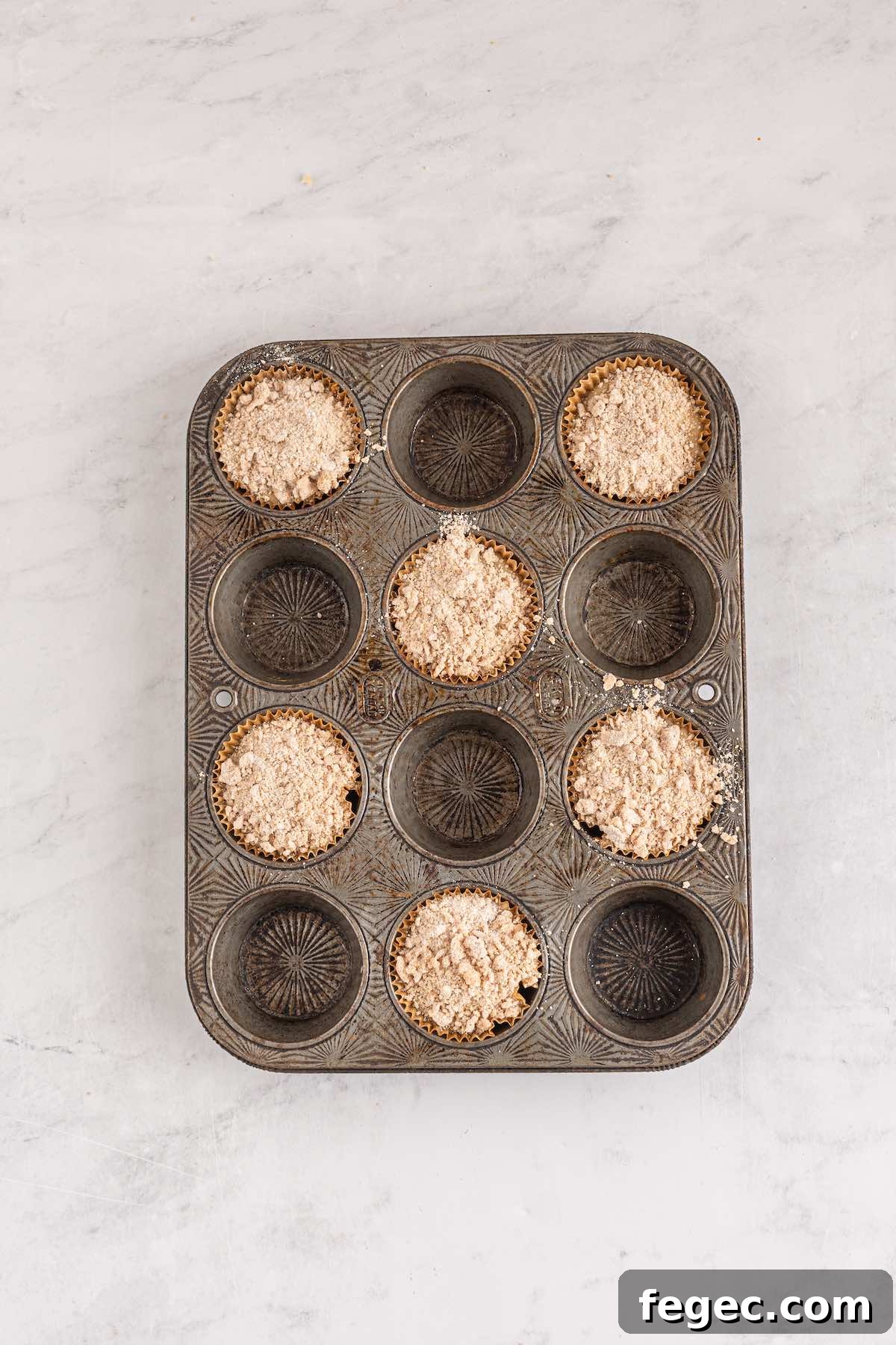 Portioned muffins in a muffin tin, topped by a spiced crumb topping.