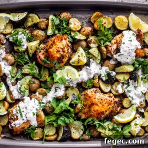 Sheet pan covered in roasted chicken thighs, zucchini, potatoes, with a drizzle of yogurt sauce and fresh herbs.
