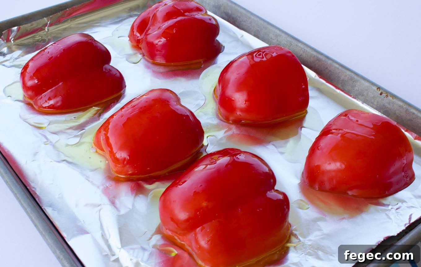 Six raw red pepper halves cut side down on a cookie sheet with olive oil