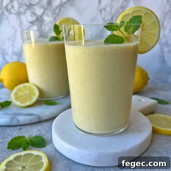Two glasses of refreshing lemon smoothie, garnished with lemon slices and mint, displayed on white boards with lemons and mint leaves scattered around.