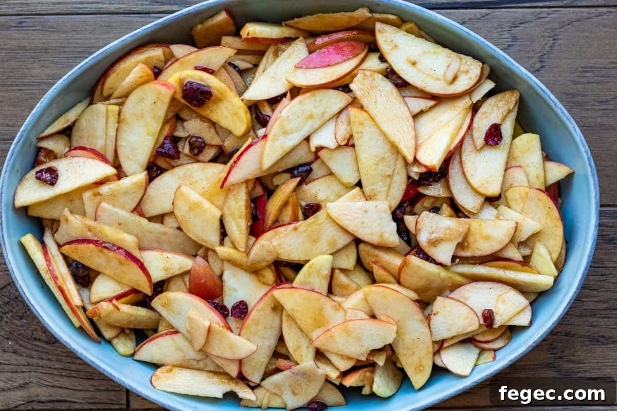 sliced apples and cranberries in a blue oval baking dish