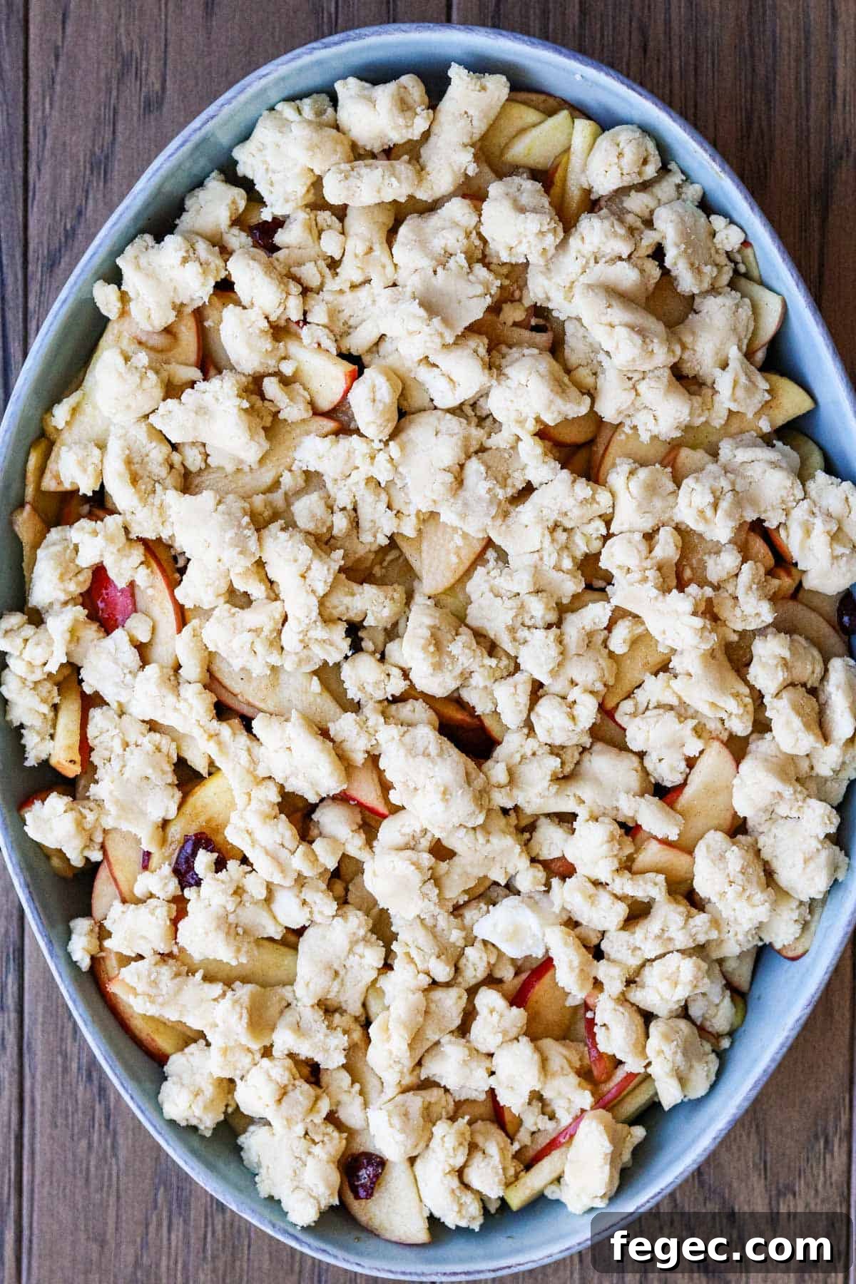 cookie dough on top of unbaked apple crisp in a blue oval baking dish