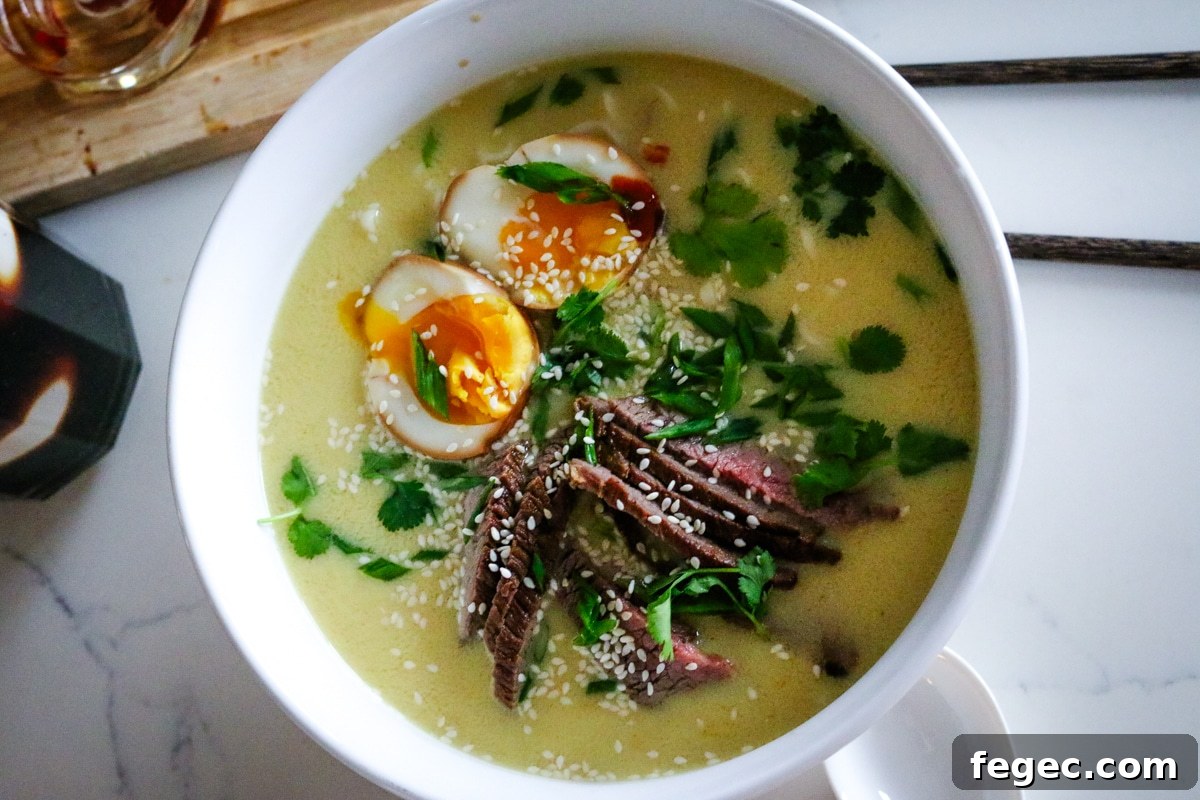 creamy ramen with soft-boiled eggs and steak in a white bowl.