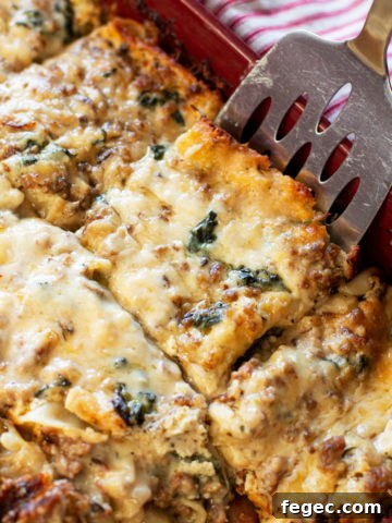 Slice of white sauce spinach lasagna on a spatula coming out of a pan.