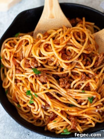 Cast iron skillet filled with person mixing spaghetti.