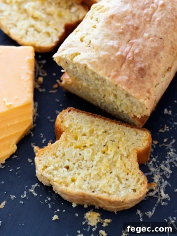 Loaf of Quick Peppery Cheese Bread sliced on a cutting board, shredded cheese on table.