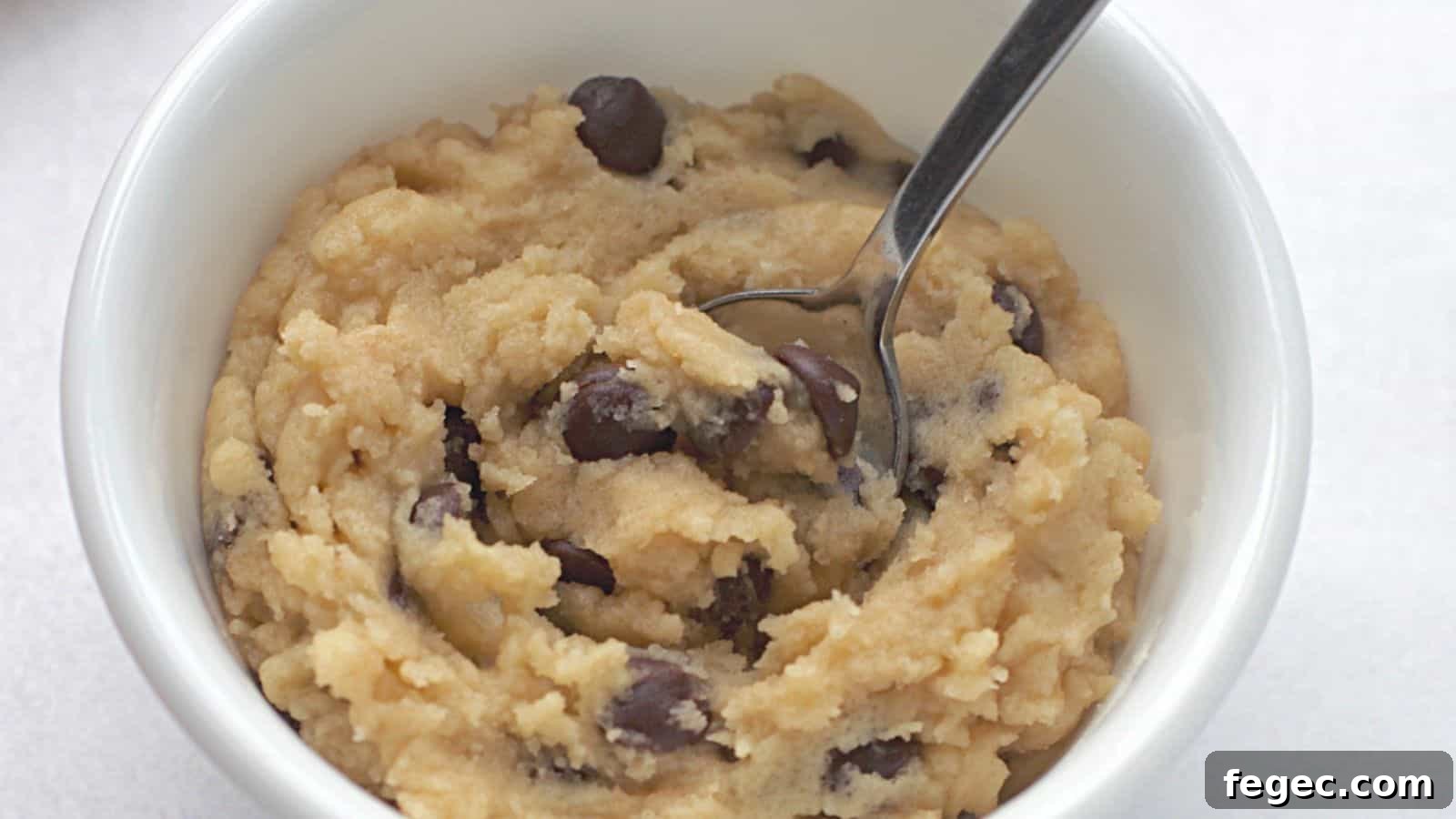 Edible chocolate chip cookie dough in white bowl with spoon.