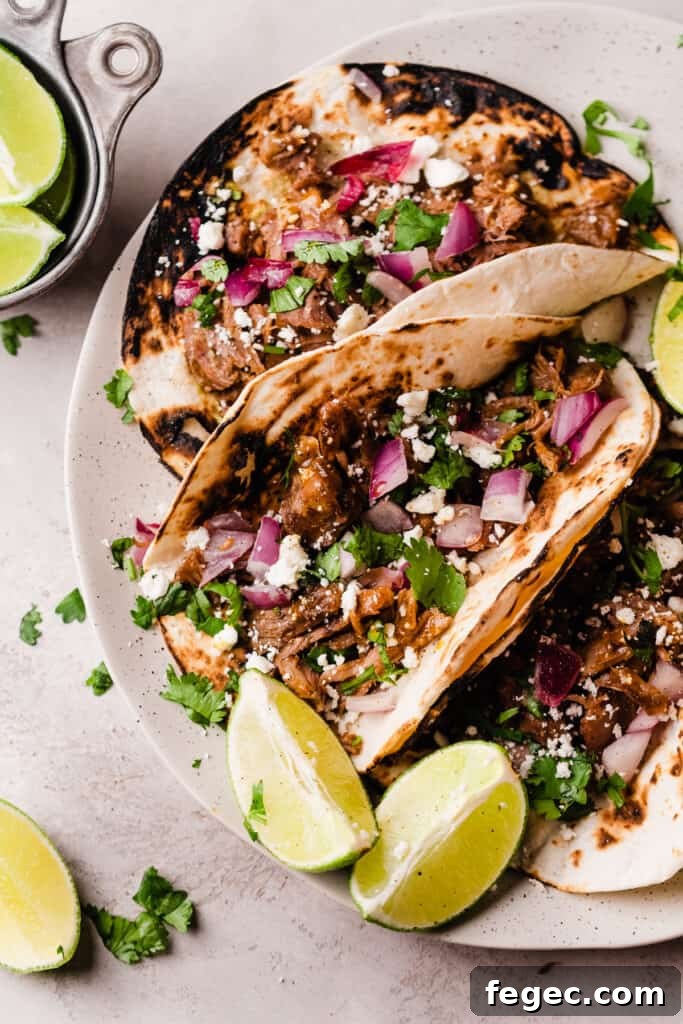 Lamb barbacoa tacos in tortillas with red onion, cotija, lime wedges, and cilantro.