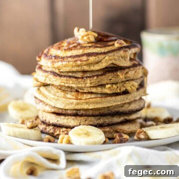 Banana oat pancakes stacked on plate with maple syrup being drizzled on top.