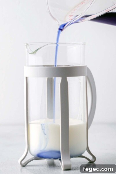 Pouring butterfly pea flower syrup into a French press with milk. 