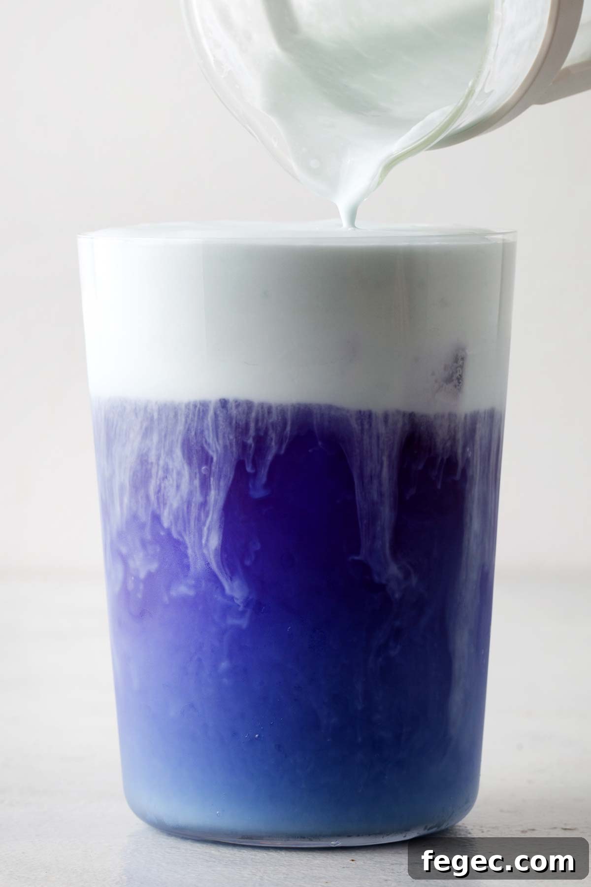 Butterfly Pea Flower Cold Foam being poured into clear glass on top of  Butterfly Pea Flower Iced Tea.