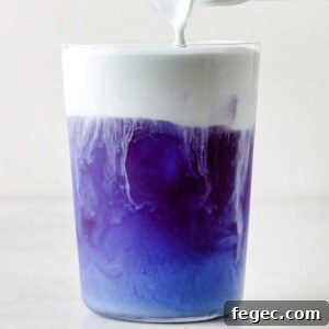 Butterfly Pea Flower Cold Foam being poured into clear glass on top of Butterfly Pea Flower Iced Tea.