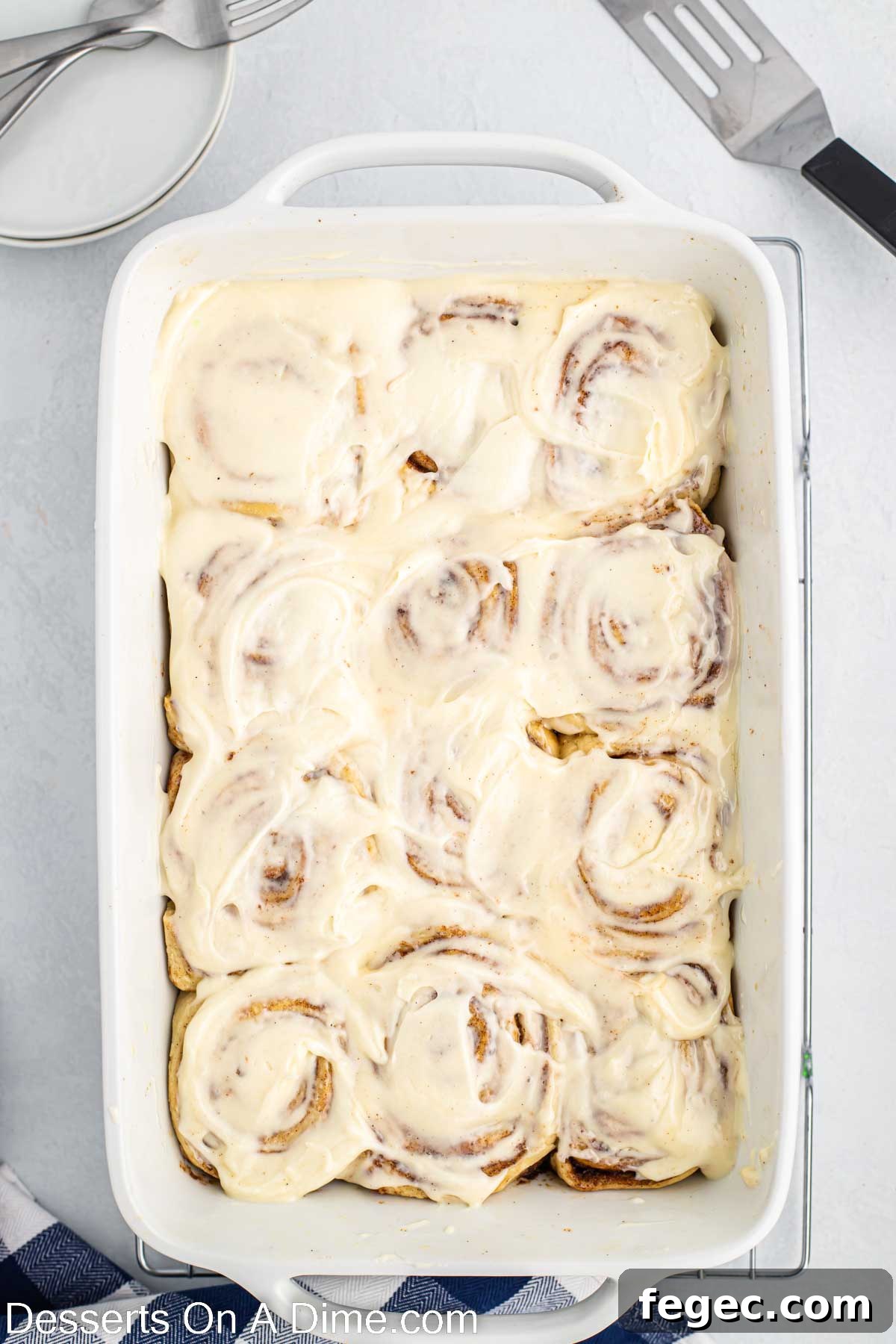 Frosting spread on cinnamon rolls in baking dish.