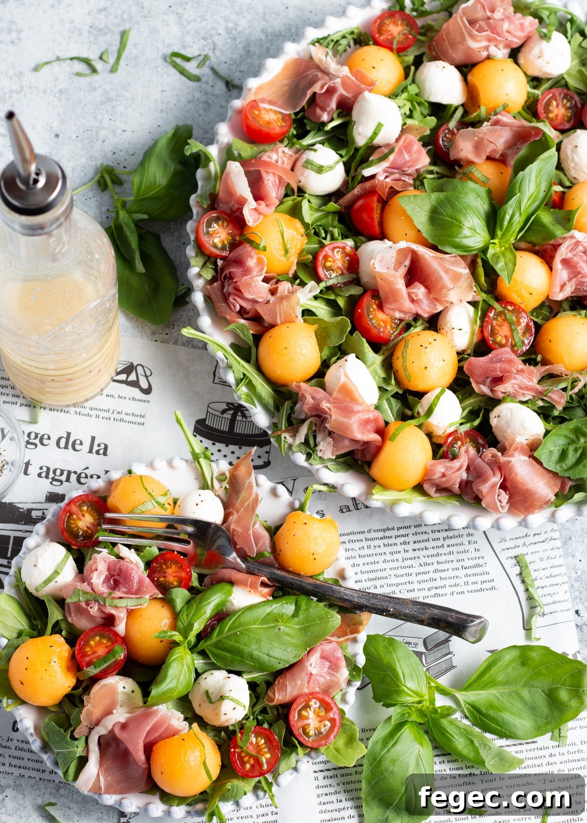 Picture of the salad in a platter and in a smaller plate too with a fork. The salad dressing is a glass bottle on the side.