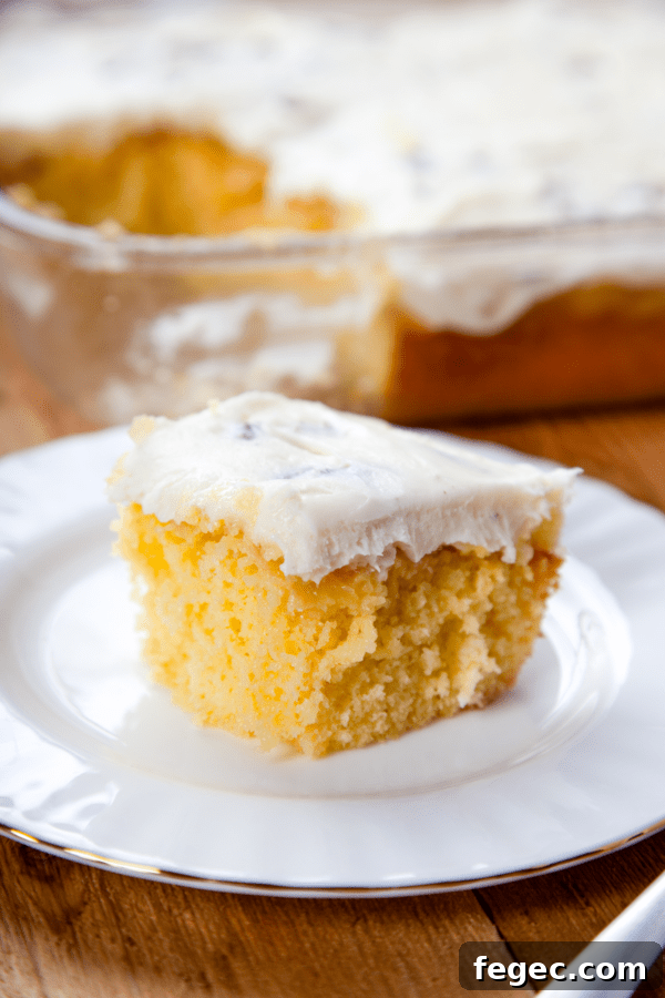 a slice of yellow pineapple cake with cream cheese icing on a white plate.