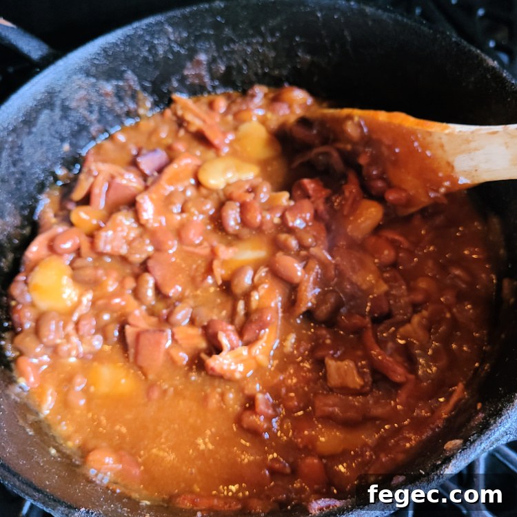 Smoked Pulled Pork Loaded Baked Beans smoking on pellet grill being stirred with wooden spoon