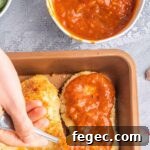 Spreading tomato sauce over breaded cutlets.