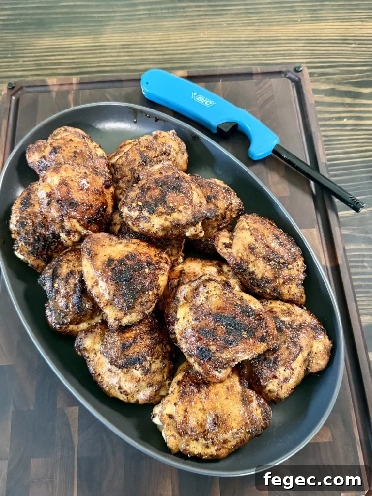 Juicy Grilled Chicken Thighs with Crispy Skin and Garlic Herb Rub 10 Honey chili crisp grilled chicken thighs with caramelized coating arranged in a dark pan on wooden cutting board